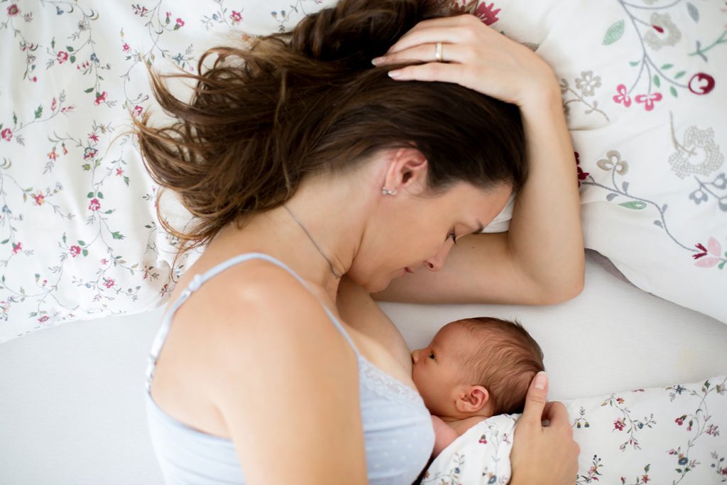 Jeune maman allaitant son bébé dans le lit