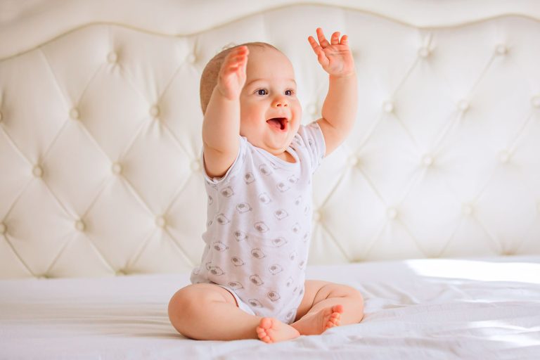 Bébé heureux et souriant assis sur un lit en levant les bras