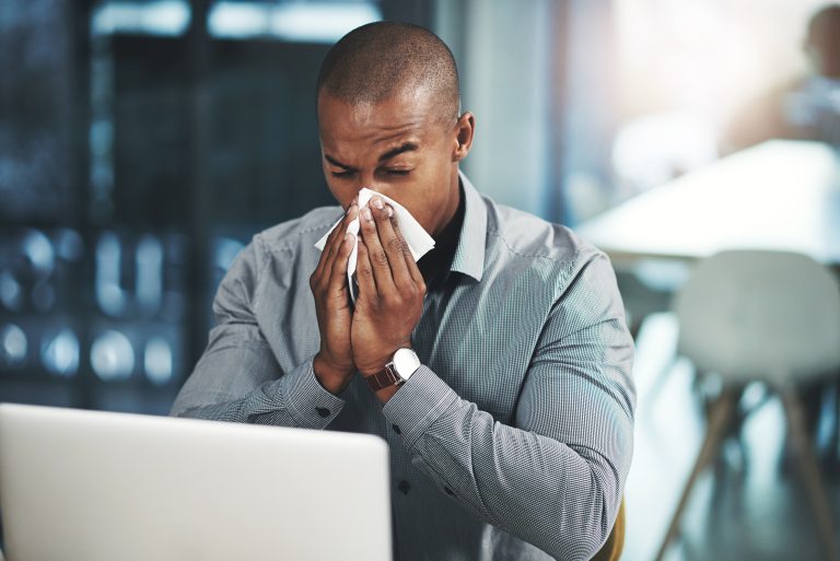 Jeune homme d'affaires au bureau devant son ordinateur en train de se moucher