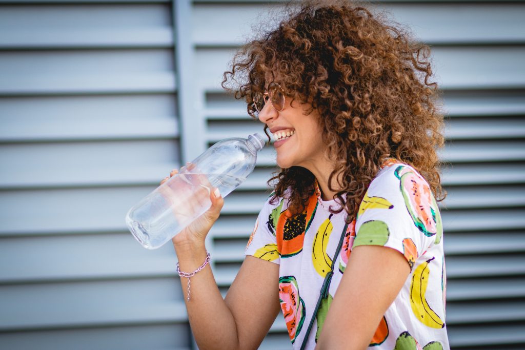 Jeune femme souriante buvant une grande bouteille d'eau en extérieur