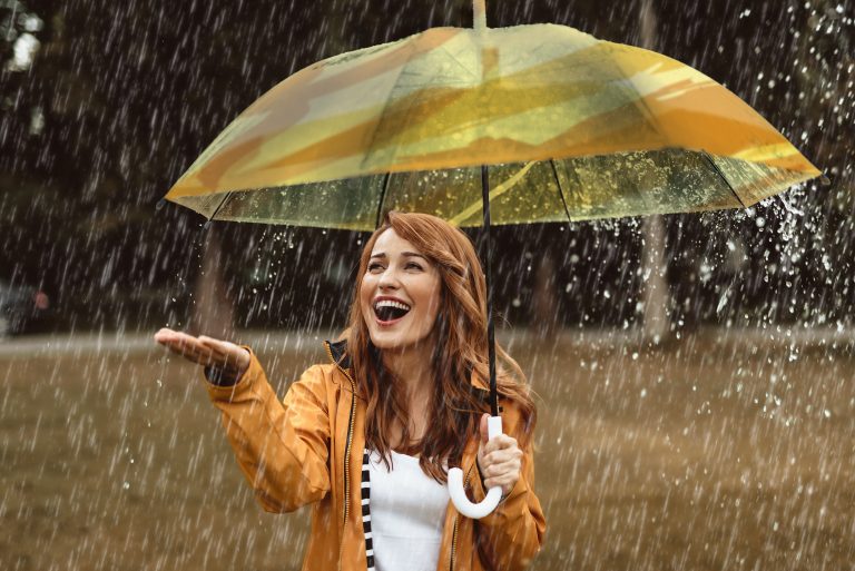 Jeune femme souriante sous parapluie jaune mettant la main sous la pluie