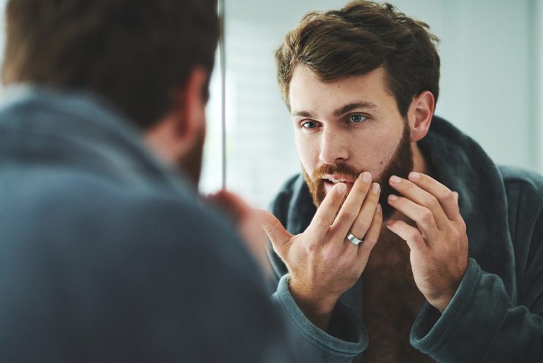 Jeune homme devant miroir observant les défauts sur sa peau