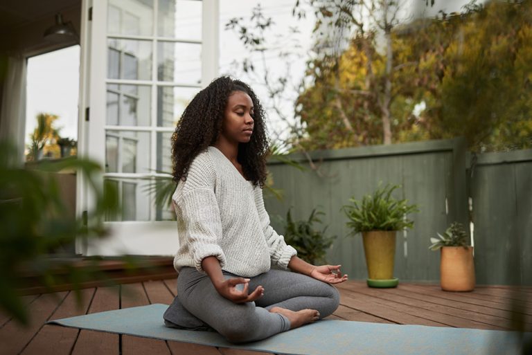 Jeune femme sur terrasse en bois pendant séance de yoga en position du lotus