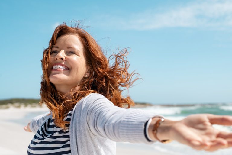 Femme souriante et heureuse les bras ouverts sur une plage au bord de la mer
