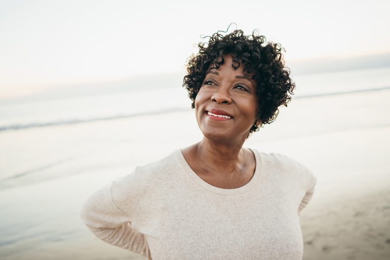 Femme souriante sur la plage au bord de l'eau prenant le temps d'admirer le paysage et de profiter du cadre