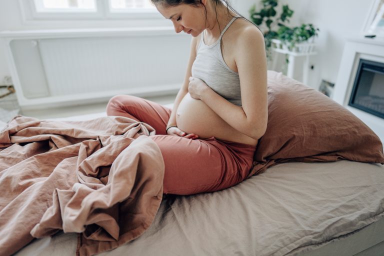 Jeune femme enceinte caressant son ventre assise dans son lit
