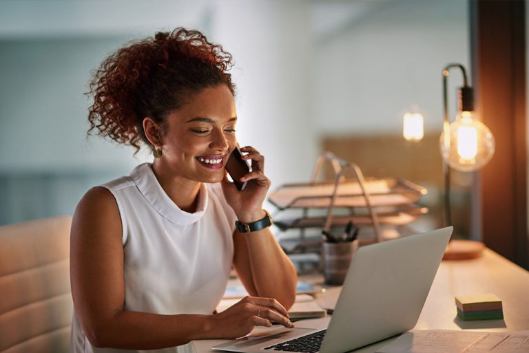 Jeune femme souriante au téléphone et au travail devant ordinateur