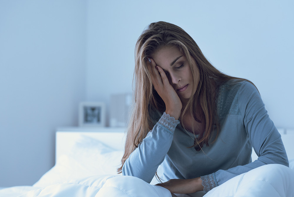 Jeune femme fatiguée qui se tient la tête au réveil dans son lit