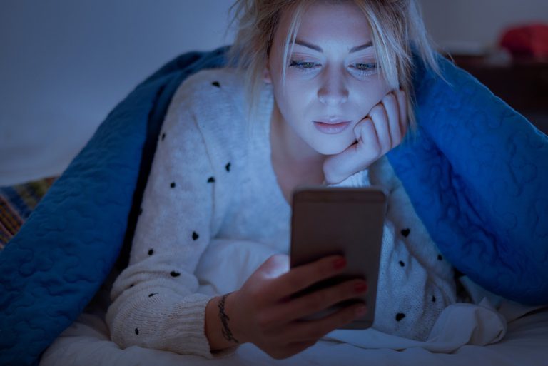 Jeune femme naviguant sur son téléphone avant de dormir
