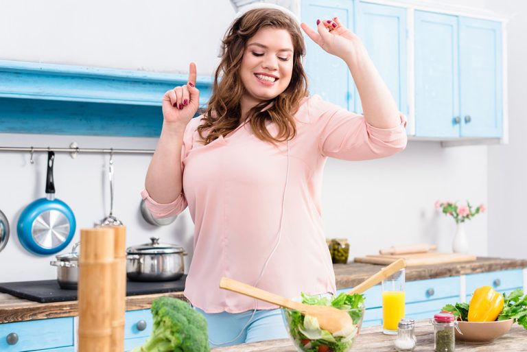 Femme joyeuse préparant une salade fraîche et écoutant de la musique dans la cuisine