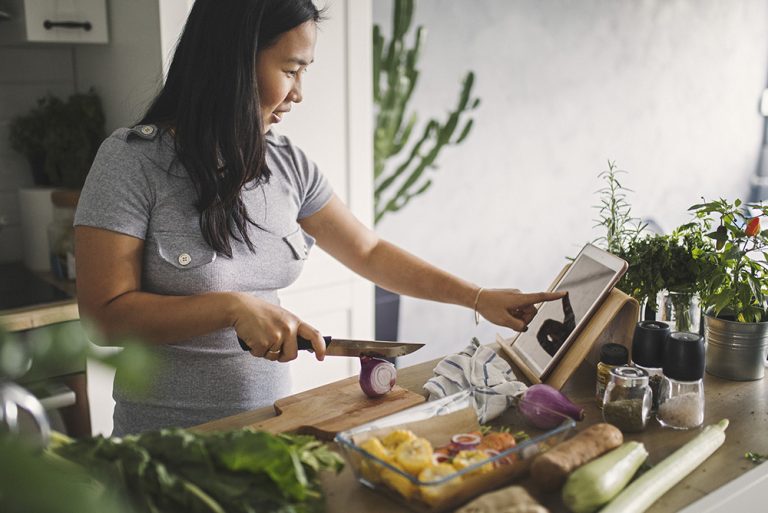 Jeune femme concoctant un plat à base de produits sains en suivant une recette en ligne sur tablette