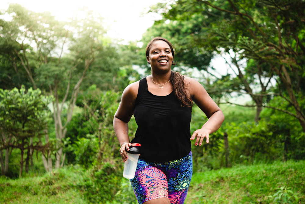Jeune femme souriante lors de sa course à pied en forêt avec gourde à la main