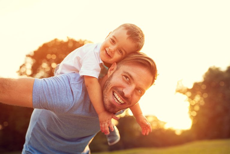 Jeune père avec son fils sur les épaules dans jardin profitant des rayons de soleil